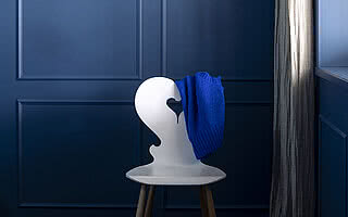 Ein stilvoller weißer Stuhl mit einem blauen Pullover auf der Rückenlehne vor einer blauen Wand.