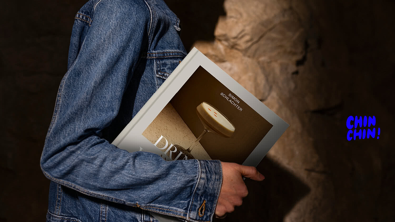 Person mit dem Cocktailbuch „Drinks we love & Food“ und Schriftzug „CHIN CHIN!“