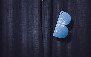 Eine Hand hält ein blaues Schild mit der Aufschrift 'Sorry for the mess' vor einem dunkelblauen Vorhang.