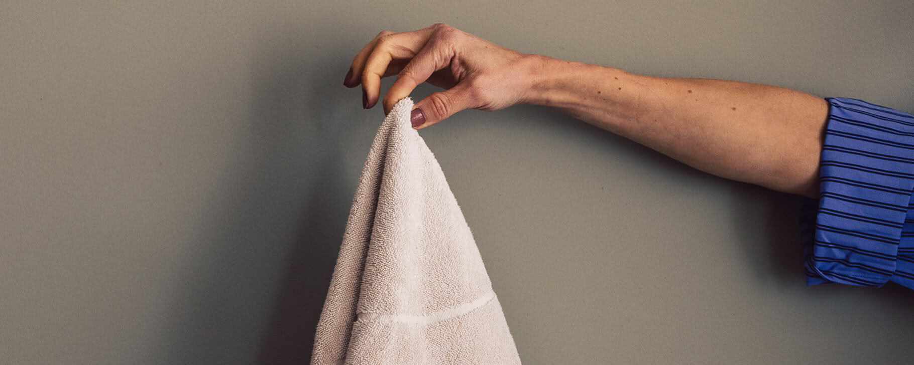 Eine Hand hält ein weiches, hellbeiges Handtuch der Blauen Burg, im Hintergrund eine graue Wand.