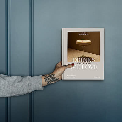 Cocktailbuch „Drinks we love & Food“ vor blauer Wand