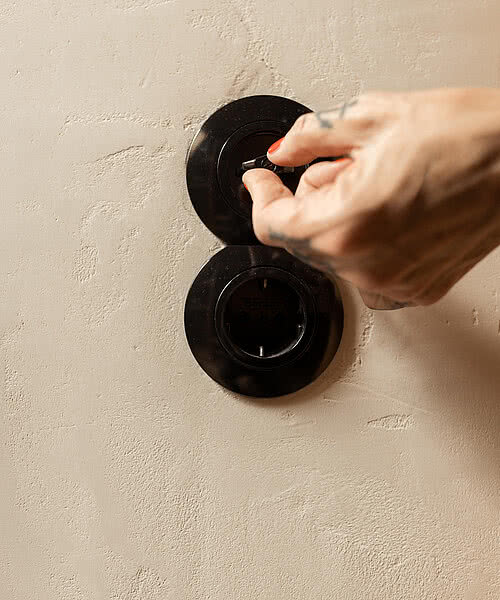 Eine Hand mit roten Nägeln schaltet den schwarzen Lichtschalter an einer beigen Wand in einem der 17 Zimmer der Blauen Burg ein